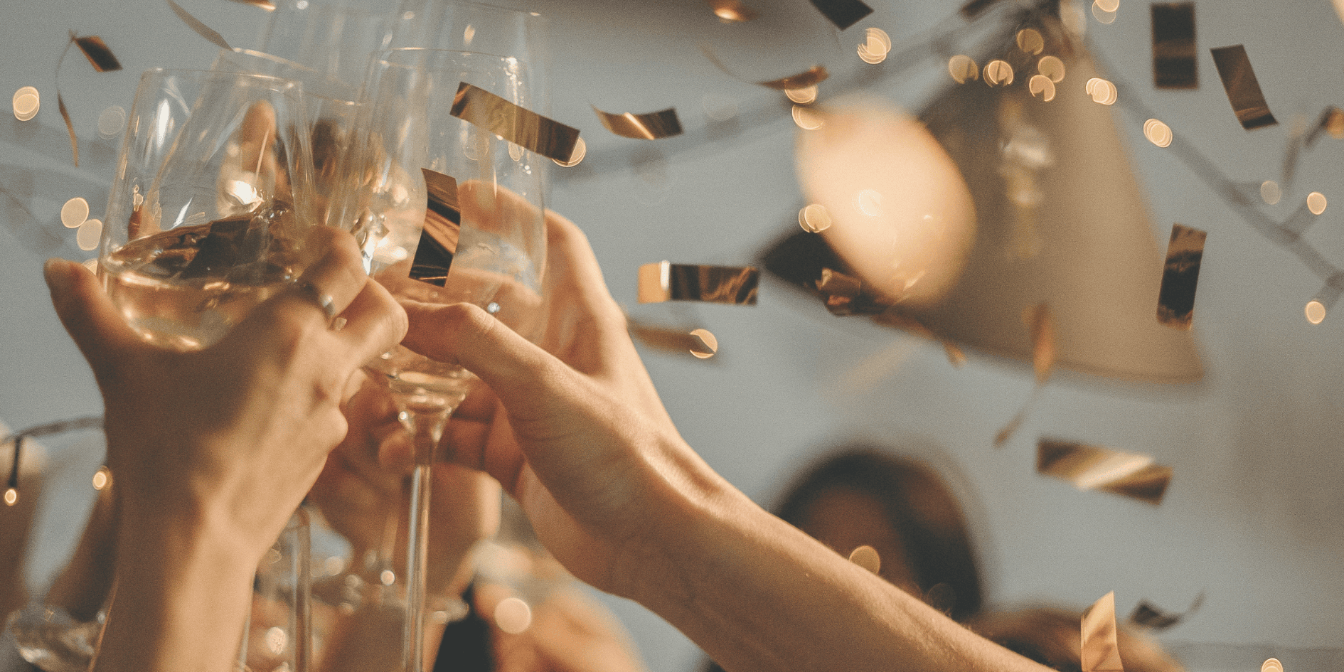 Hands in a cheers motion with glasses of wine and gold confetti falling